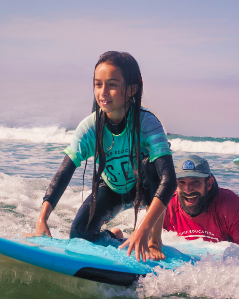 Sean Brody riding wave to help surfer catch their first wave at surf camp